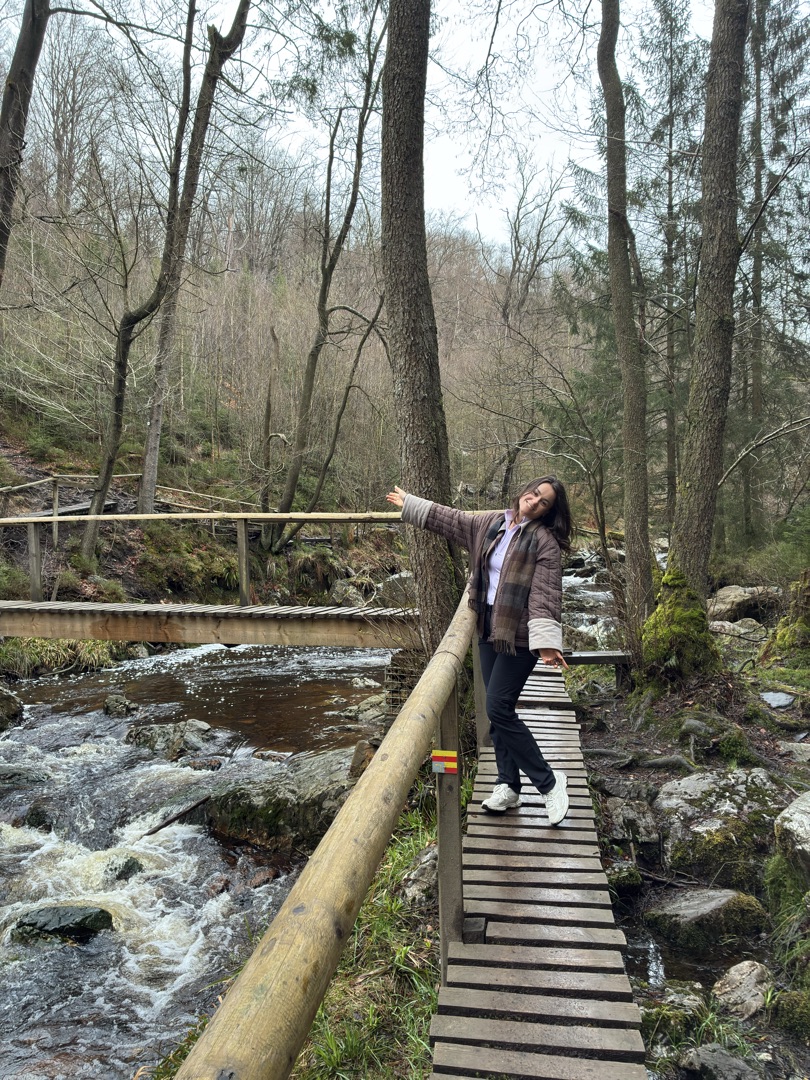 Konxhe on a wooden bridge over a rushing stream in an autumn forest