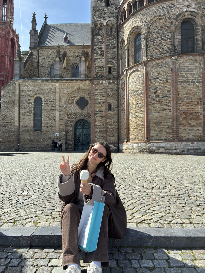Konxhe sitting on the steps of Aachen Cathedral with an ice cream, peace sign